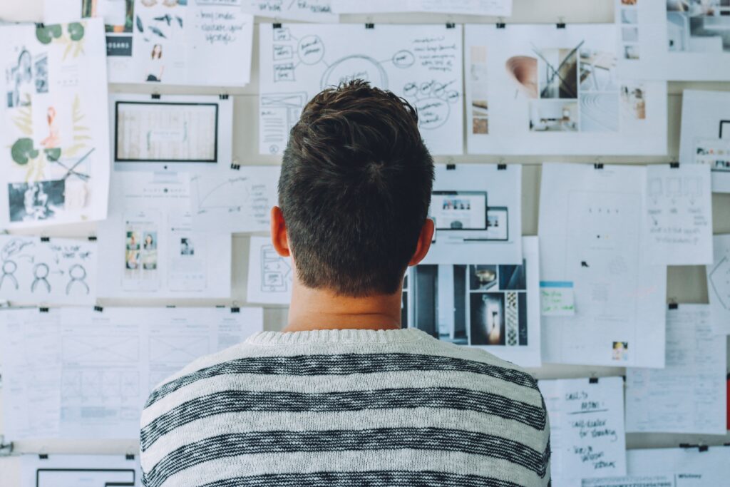 man looking at a board strewn with papers and diagrams of different designs and ideas